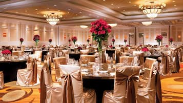 A banquet hall with round tables, chairs with brown sashes, and chandeliers.