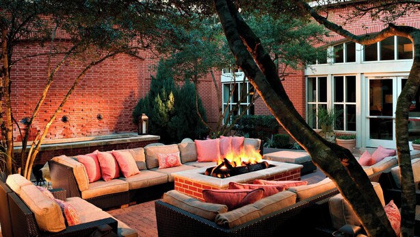 An outdoor seating area with a fire pit, wicker furniture, and a brick wall in the background. - Houston Marriott Sugar Land (Sugar Land)