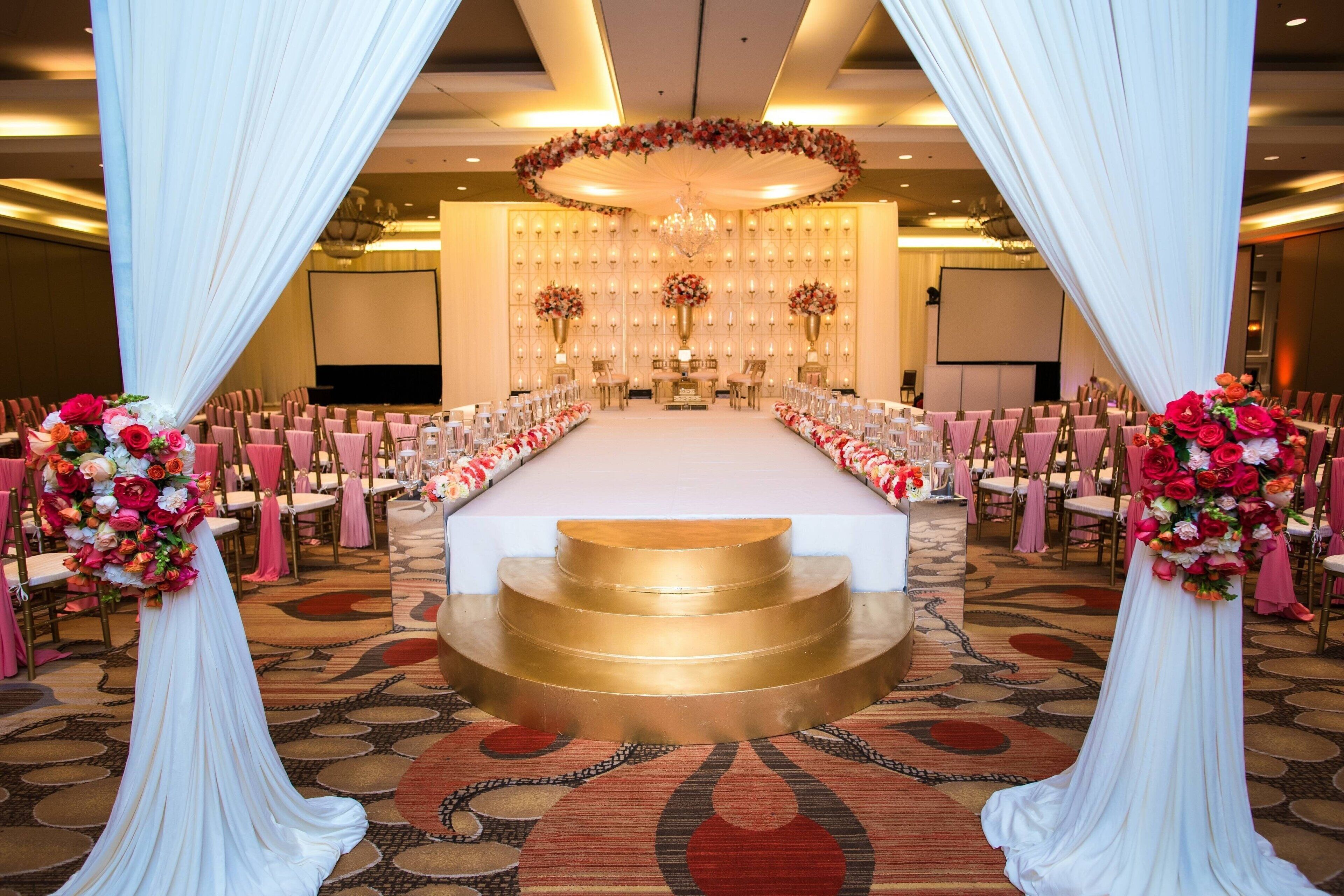 A banquet hall with a long table, chairs, and floral arrangements.