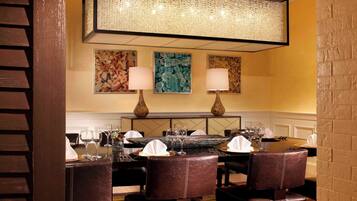 A dining area with leather chairs, a round table, and two wall-mounted lamps.