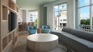 A modern living room with a large sofa, two armchairs, a round coffee table, and a TV on a wooden shelving unit.