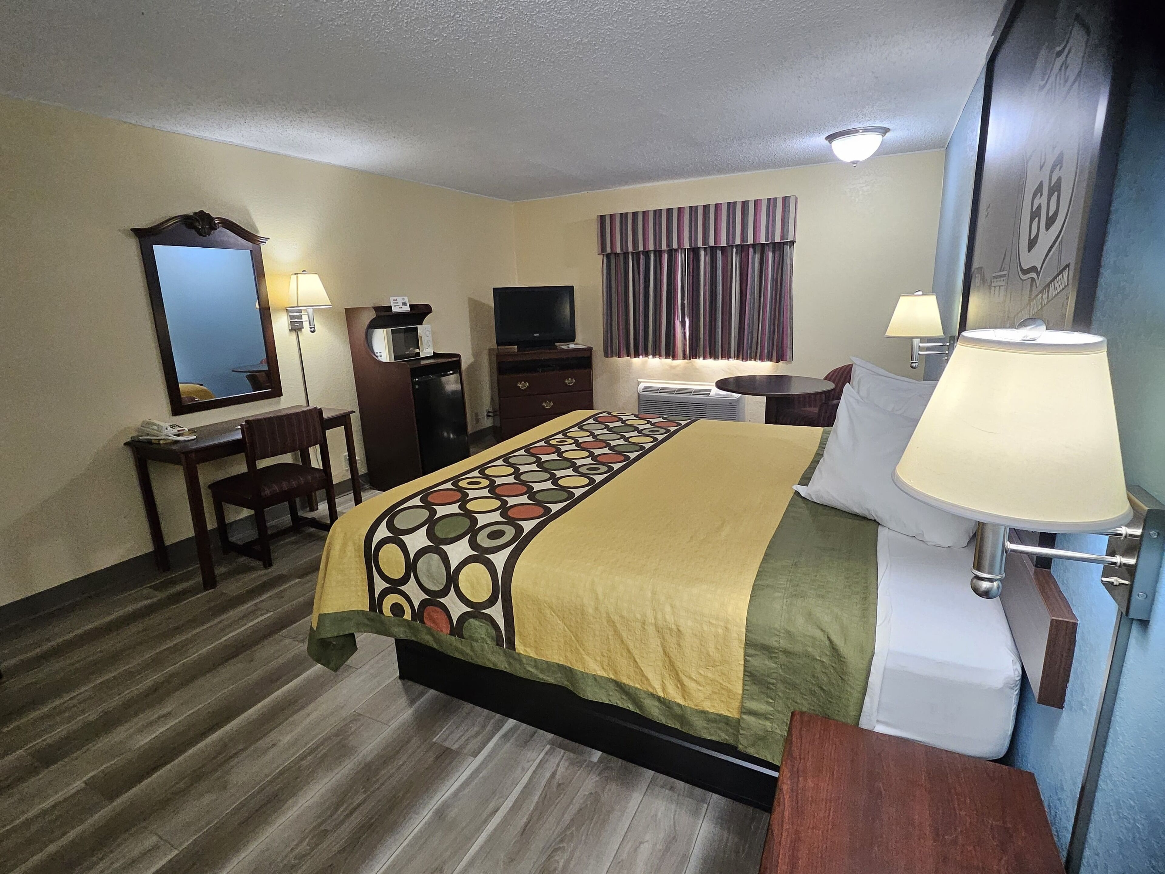 A hotel room with a bed, a desk, a chair, a TV, a lamp, and a window with curtains.
