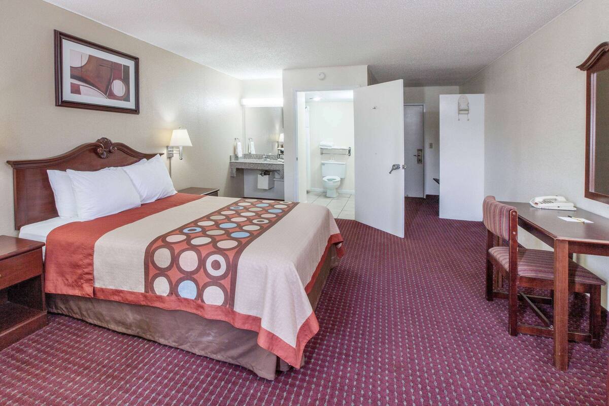 A hotel room with a bed, a desk, a chair, a bathroom, and a door leading to another room.