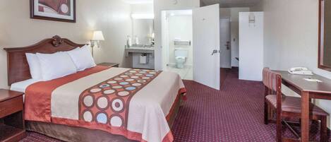 A hotel room with a bed, a desk, a chair, a bathroom, and a door leading to another room.