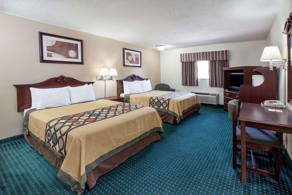 A hotel room with two beds, a desk, a chair, a TV, and a window with curtains.