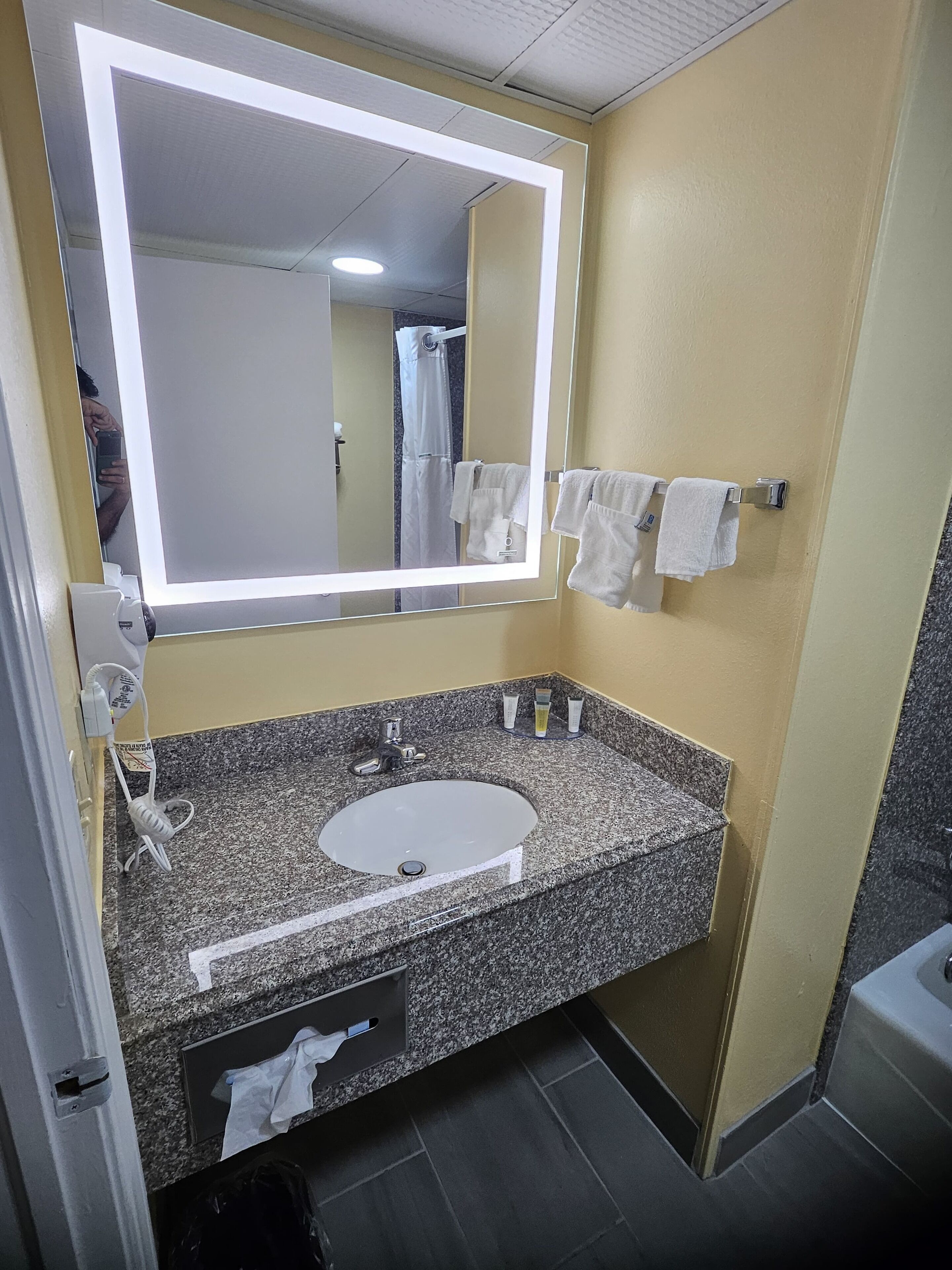 Casa de banho com bancada de granito, lavatório branco, espelho com luz e porta-toalhas com duas toalhas.