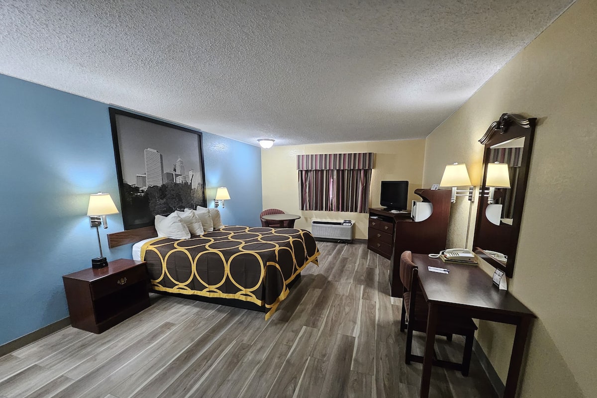 A hotel room with a bed, bedside tables, a desk, a chair, a television, and a mirror.
