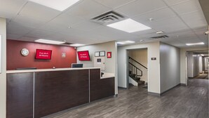A reception area with a wooden reception desk, two red monitors displaying 'Free Wi-Fi All Rooms,' and a clock on the wall.