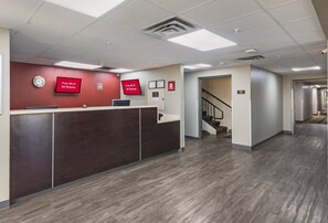 A reception area with a wooden reception desk, two red monitors displaying 'Free Wi-Fi All Rooms,' and a clock on the wall. - Red Roof Inn & Suites Austin East - Manor (Manor)