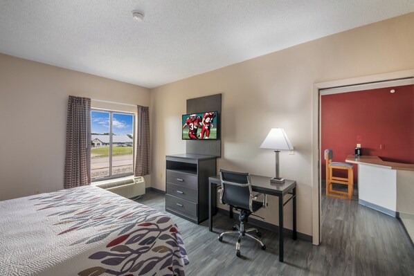 A hotel room with a bed, desk, chair, TV, and a view of the outdoors.