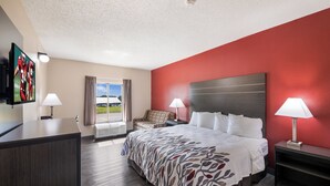 A hotel room with a bed, two bedside lamps, a television on the left, a window with curtains, and a red accent wall. - Red Roof Inn & Suites Austin East - Manor (Manor)