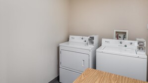 A laundry room with two Whirlpool washers and dryers, a wooden table, and a wall-mounted electrical outlet.