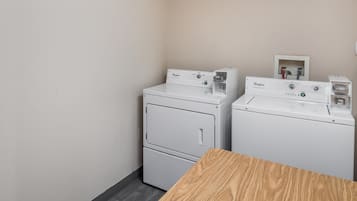 A laundry room with two Whirlpool washers and dryers, a wooden table, and a wall-mounted electrical outlet.
