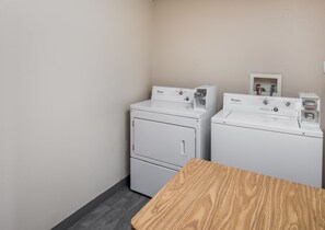 A laundry room with two Whirlpool washers and dryers, a wooden table, and a wall-mounted electrical outlet. - Red Roof Inn & Suites Austin East - Manor (Manor)
