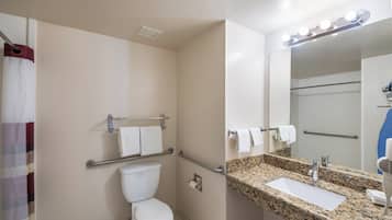 Een badkamer met toilet, grepen, een wastafel met granieten blad en een spiegel met verlichting erboven.