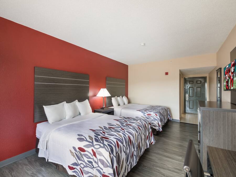 A hotel room with two beds, a desk, a TV, and a red accent wall.
