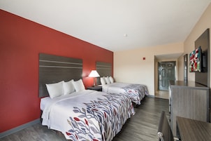 Habitación de hotel con dos camas, un escritorio, un televisor y una pared decorada en rojo.