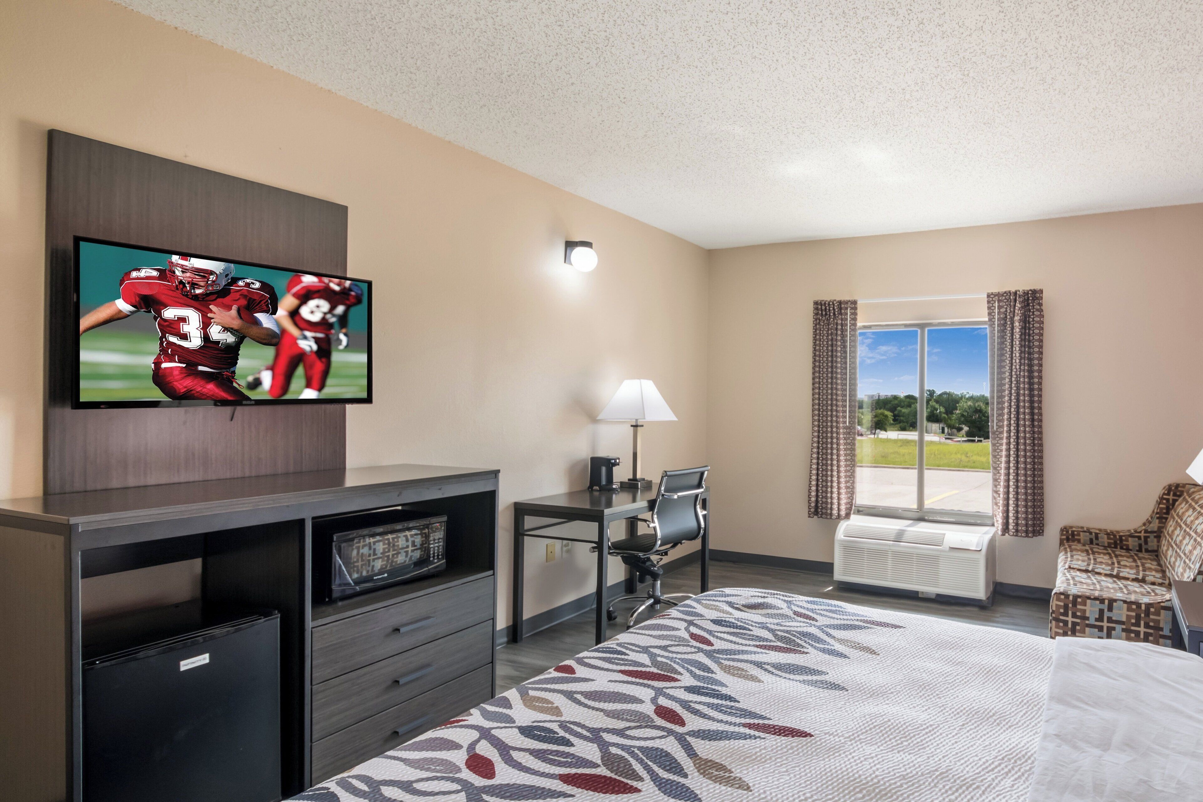 A hotel room with a bed, a desk, a television, a chair, and a window with curtains.