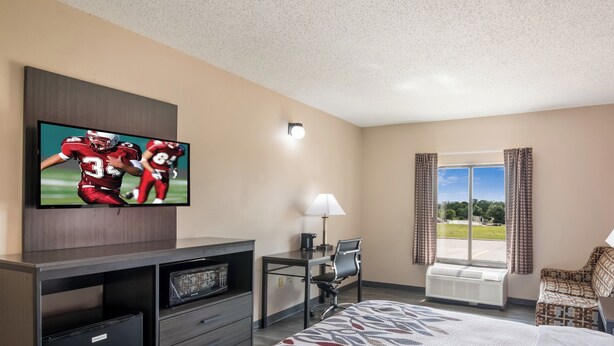A hotel room with a bed, a desk, a television, a chair, and a window with curtains.
