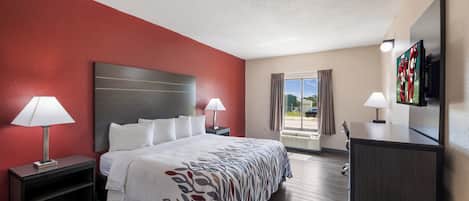 Quarto de hotel com cama, duas mesas de cabeceira com abajures, televisão e janela com cortinas.