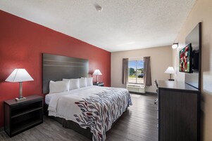 Habitación de hotel con cama, dos mesitas de noche con lámparas, un televisor y una ventana con cortinas.