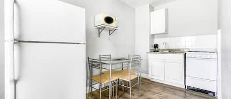 A compact kitchen with white cabinets, a built-in oven, and a small dining area with a glass table and metal chairs.