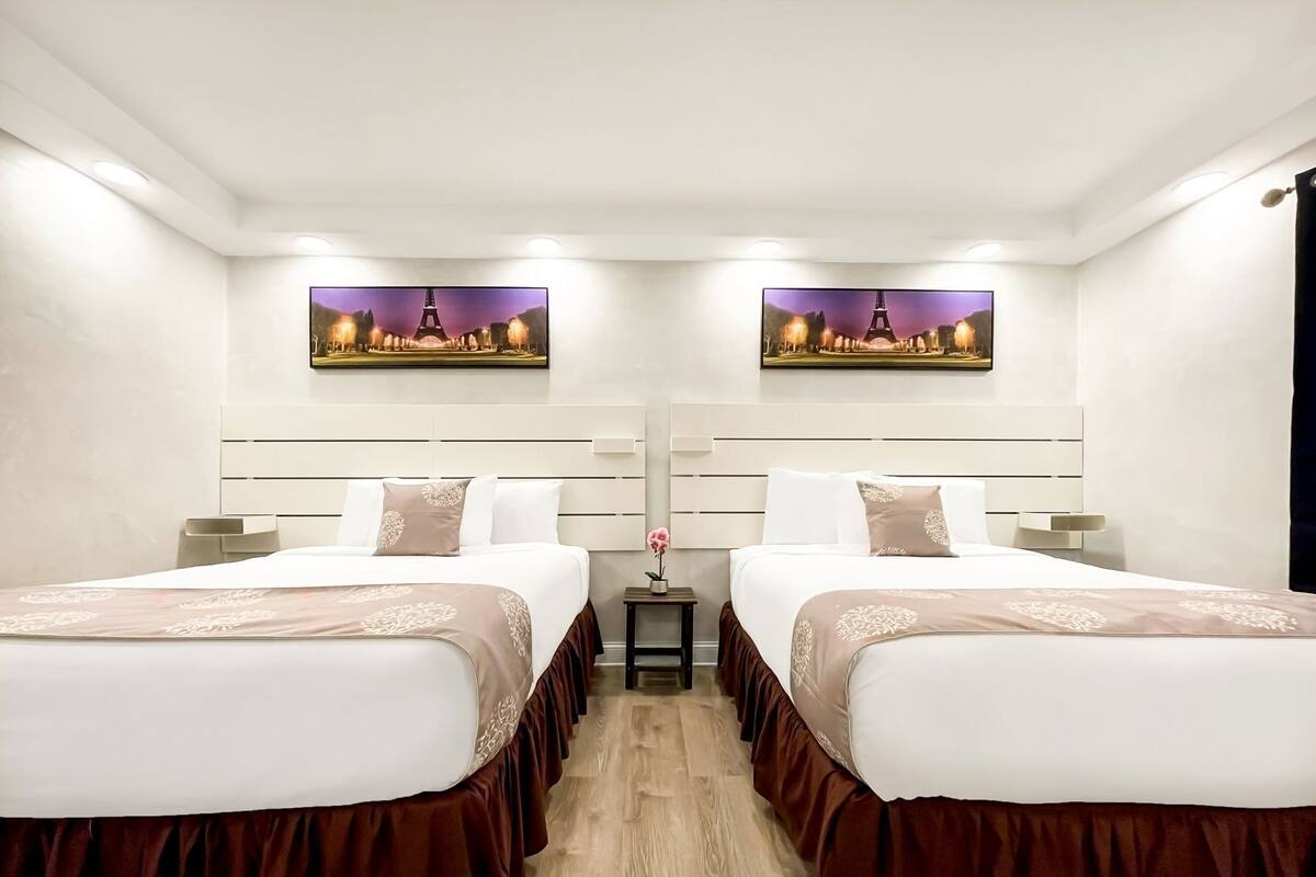 A hotel room with two beds, a small table, and a wall-mounted TV.