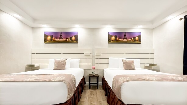 Una habitación de hotel con dos camas, cada una con cabecera, una mesita con un florero y dos cuadros colgados en la pared.