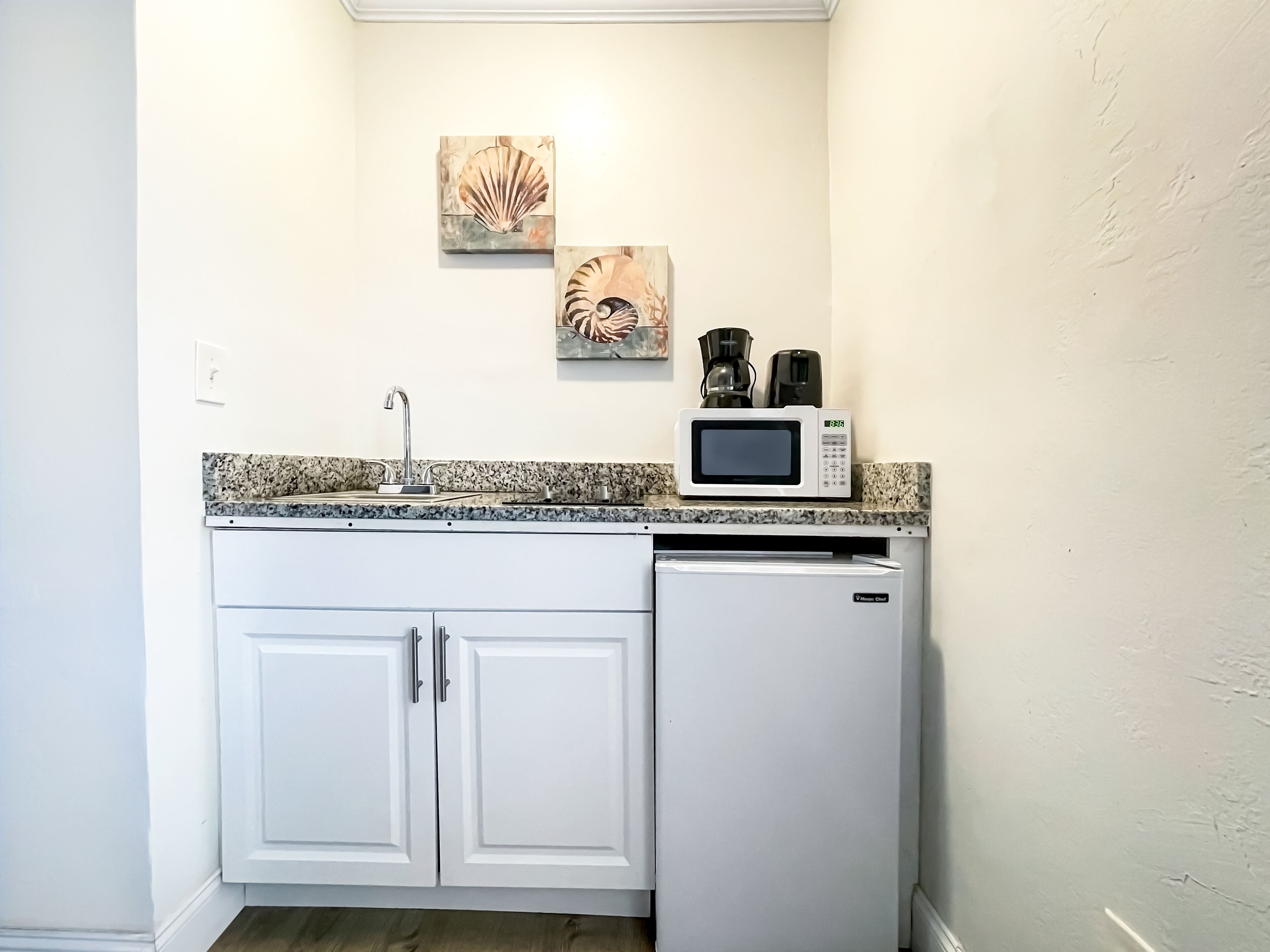 A compact kitchen with white cabinetry, a granite countertop, a microwave, and a coffee maker.