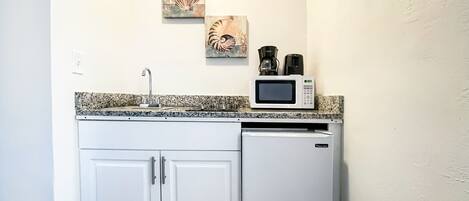 A compact kitchen with white cabinetry, a granite countertop, a microwave, and a coffee maker.