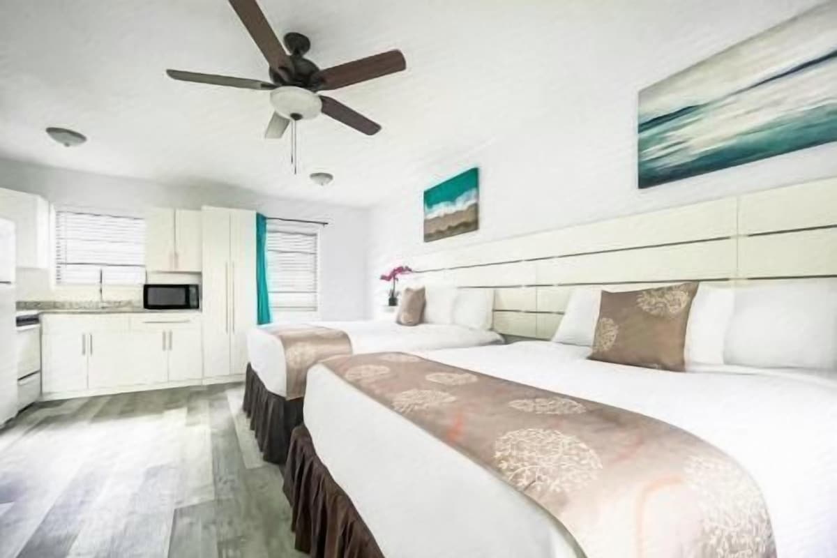 A hotel room with a large bed, a ceiling fan, a television, and a painting on the wall.