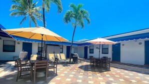Un patio con suelo de baldosas, mobiliario exterior y palmeras.
