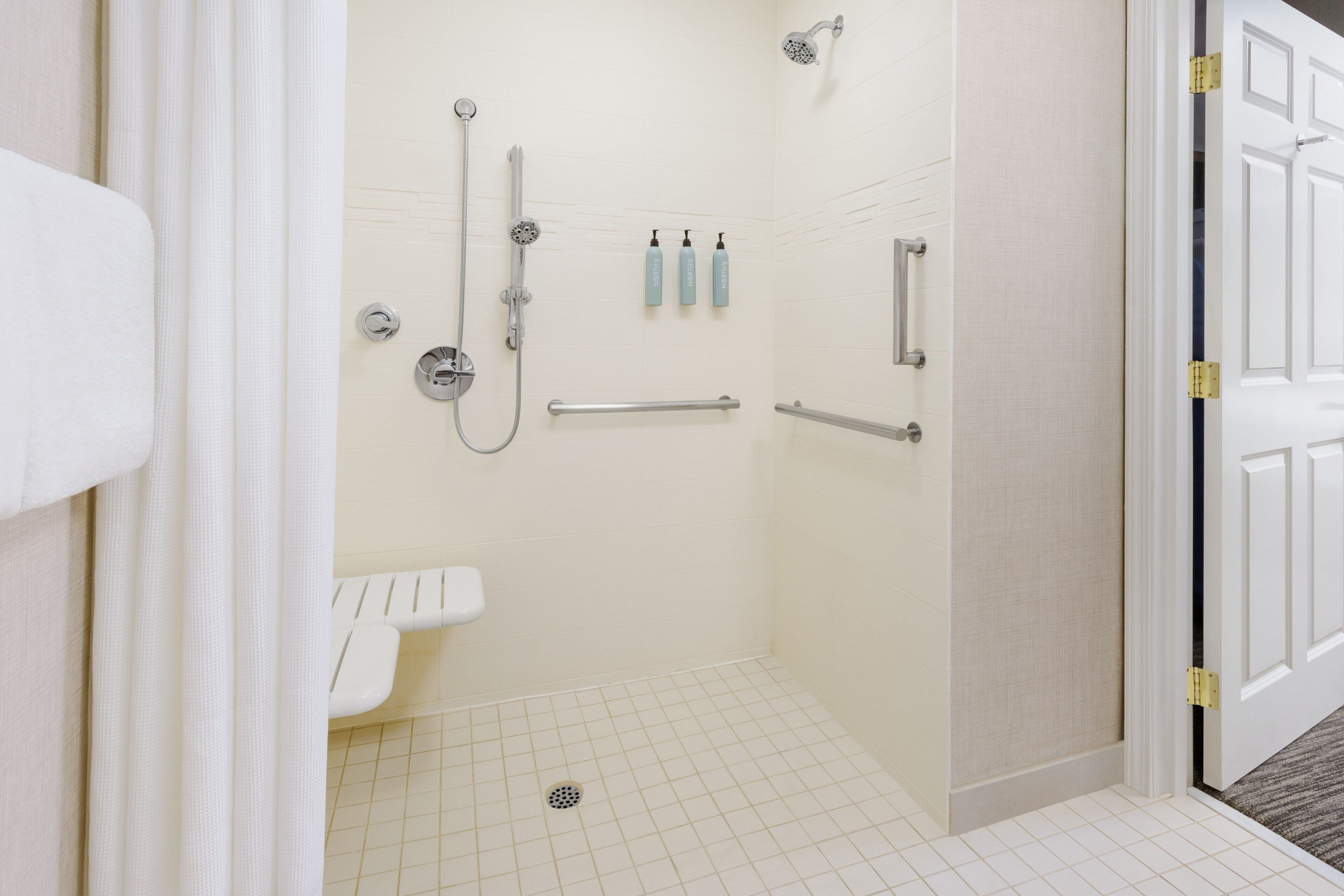 A bathroom with a shower, toilet, and sink. There are three bottles on the wall.