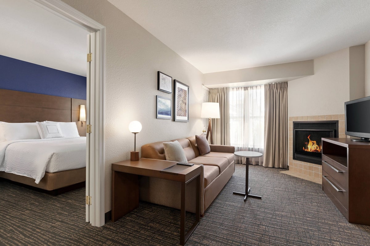A hotel room with a bed, a sofa, a small table, a TV, and a fireplace.