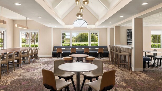 A spacious conference room with a high ceiling, multiple tables and chairs, a central seating area, and large windows providing natural light. - Residence Inn by Marriott Salinas Monterey (Salinas)