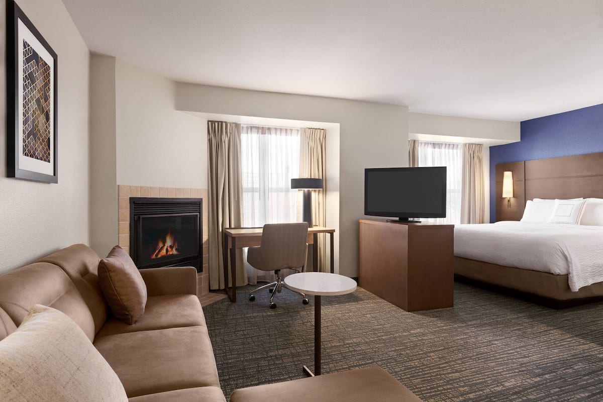 A hotel room with a sofa, a TV, a bed, a small table, a chair, a fireplace, and curtains.