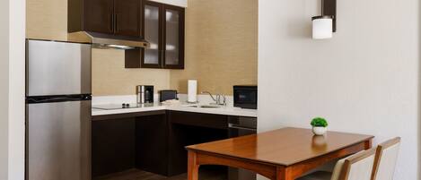 Una cocina compacta equipada con refrigerador, microondas, pileta y una mesa de madera con sillas.