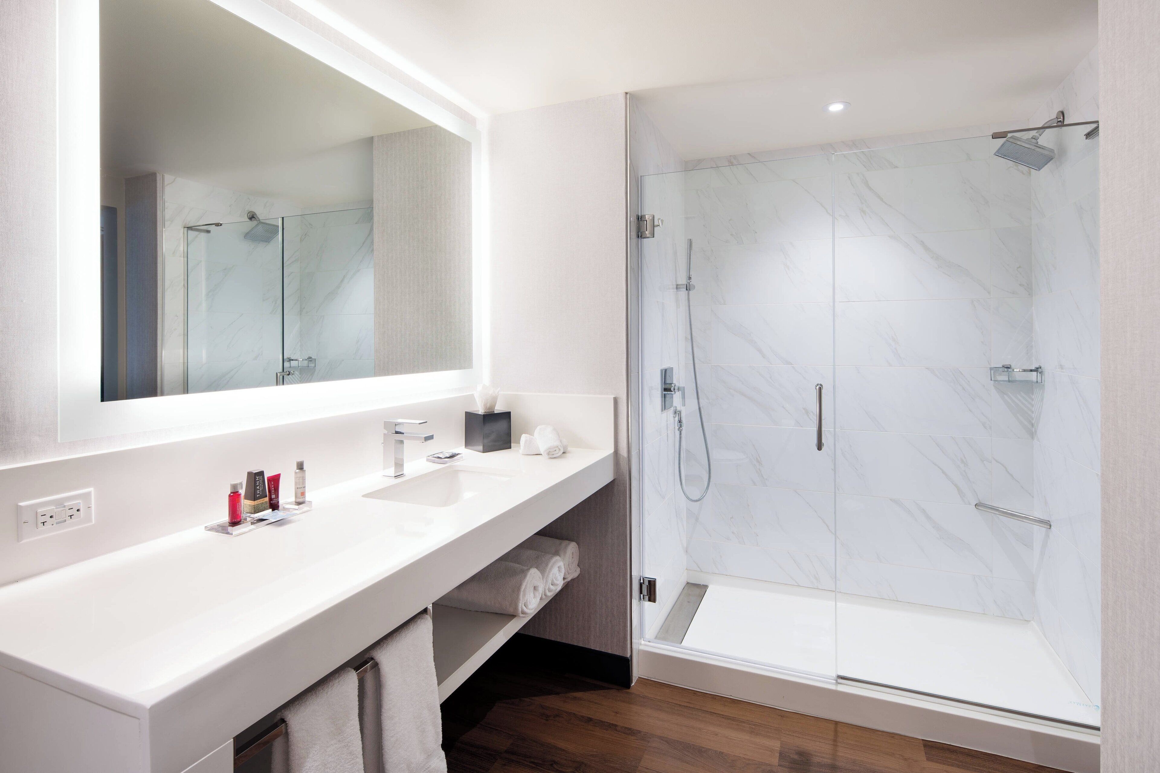 A modern bathroom with a large mirror, white countertop, and a glass-enclosed shower.