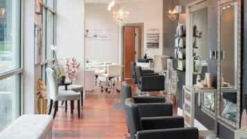 Un salón de belleza con varias estaciones de peluquería, una recepción y un espejo grande.