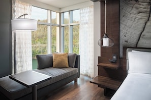 A modern room with a sofa, a small table, a bed, and a large window with curtains.