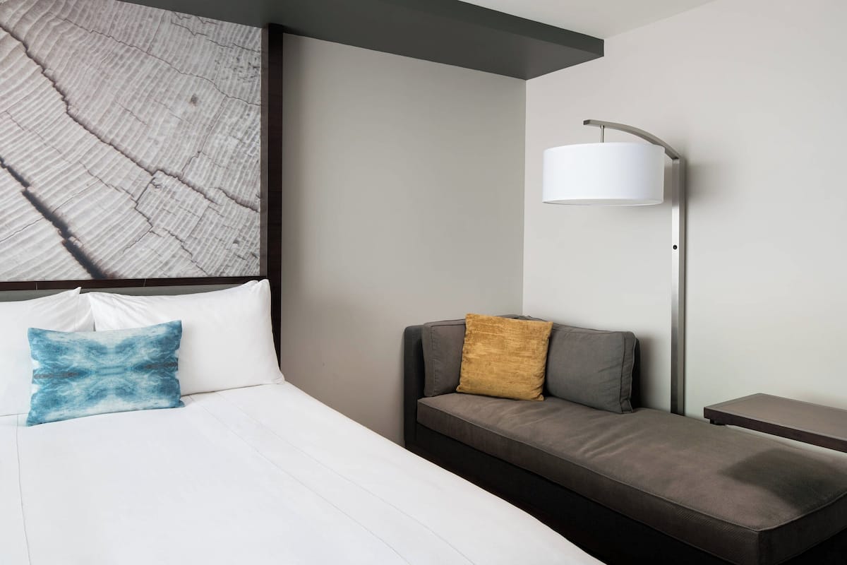 Ein modernes Hotelzimmer mit Bett, Sofa, Nachttisch und Lampe.