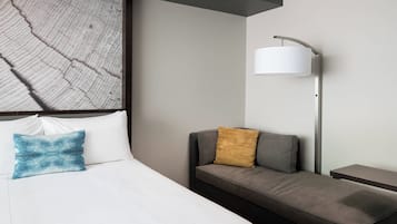 Una habitación de hotel moderna con cama, sofá, mesita de noche y lámpara.