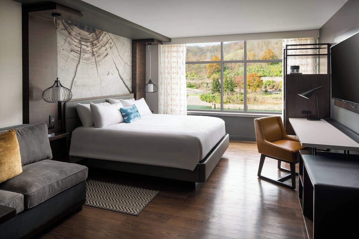 Ein modernes Schlafzimmer mit einem großen Bett, einem Schreibtisch und Blick auf einen Wald durch ein großes Fenster.