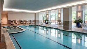 An indoor swimming pool with lounge chairs and tables, surrounded by large windows and potted plants. - Morgantown Marriott at Waterfront Place (Morgantown)