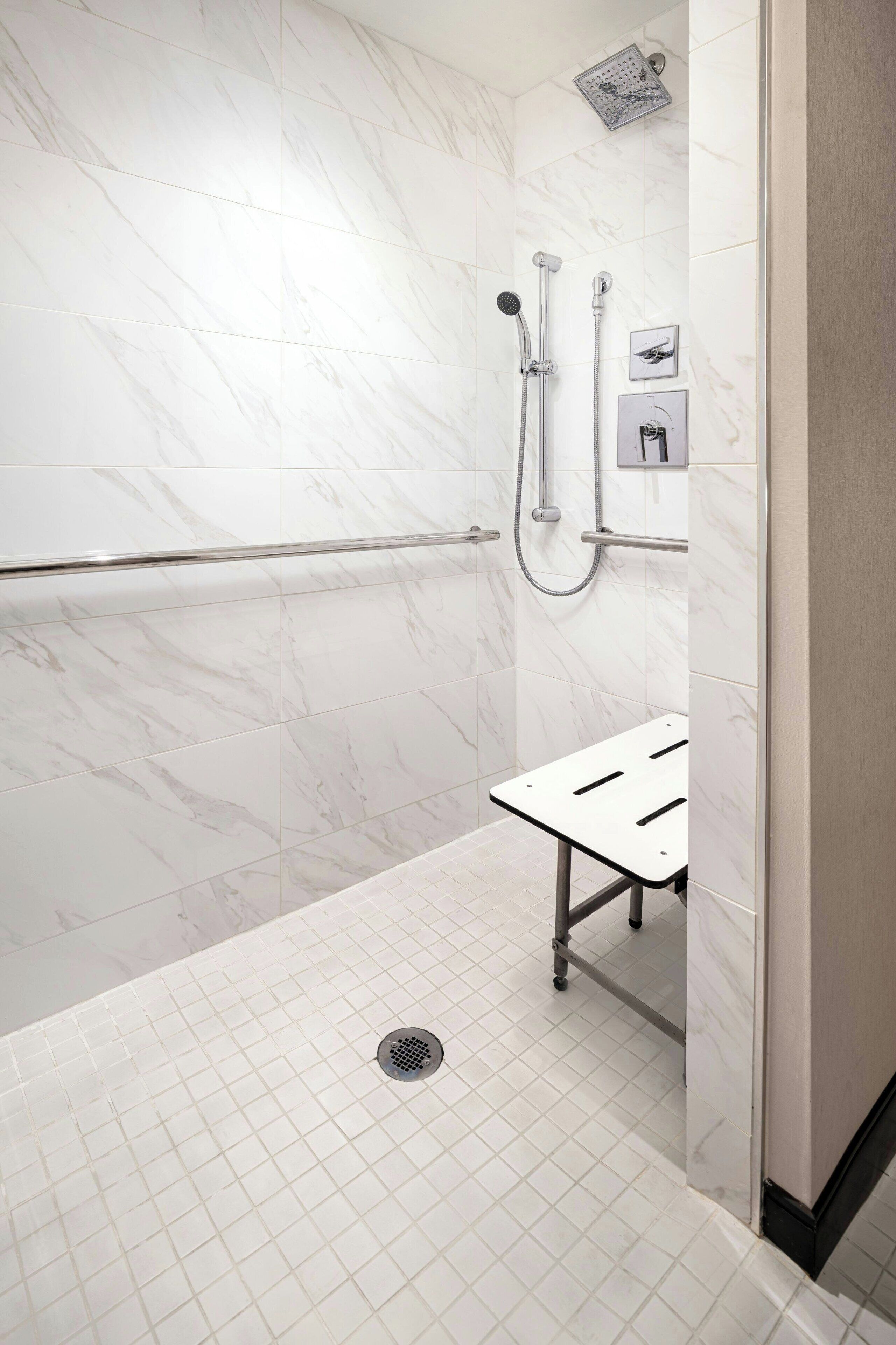 Un baño moderno con baldosas de mármol blanco, cabina de ducha de vidrio, cabezal de ducha manual y toallero.