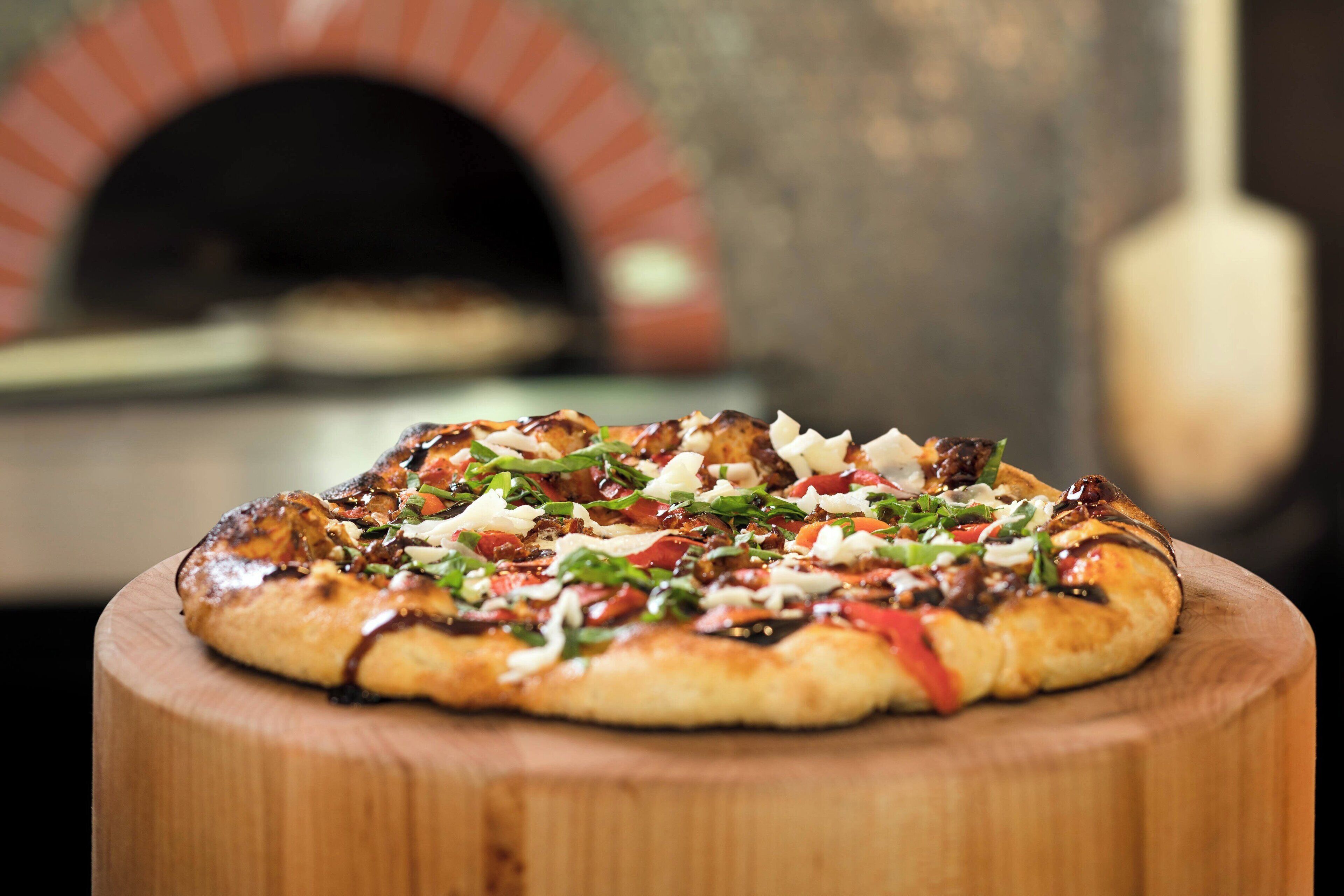 A pizza on a wooden board with a brick oven in the background.
