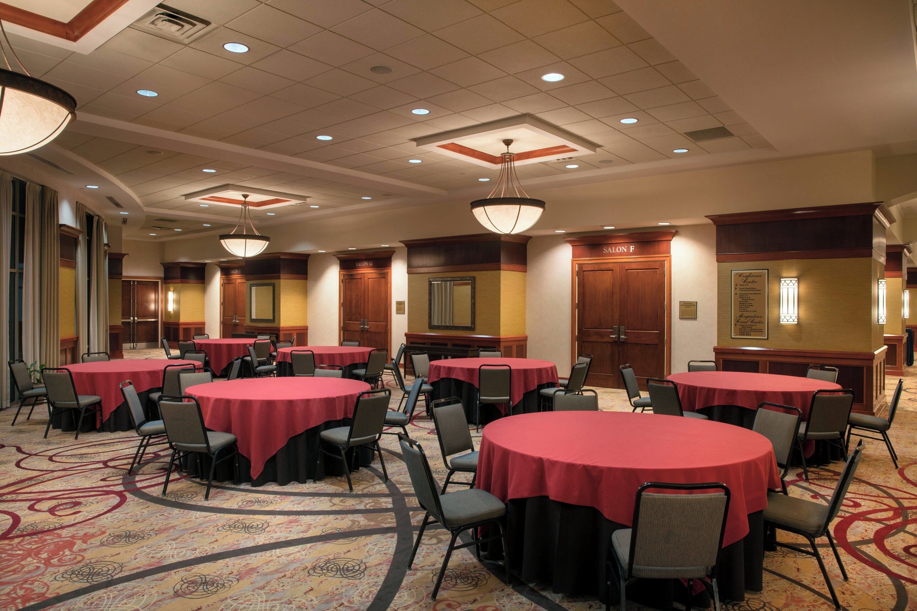 A conference room with multiple round tables covered with red tablecloths, arranged in a U-shape.