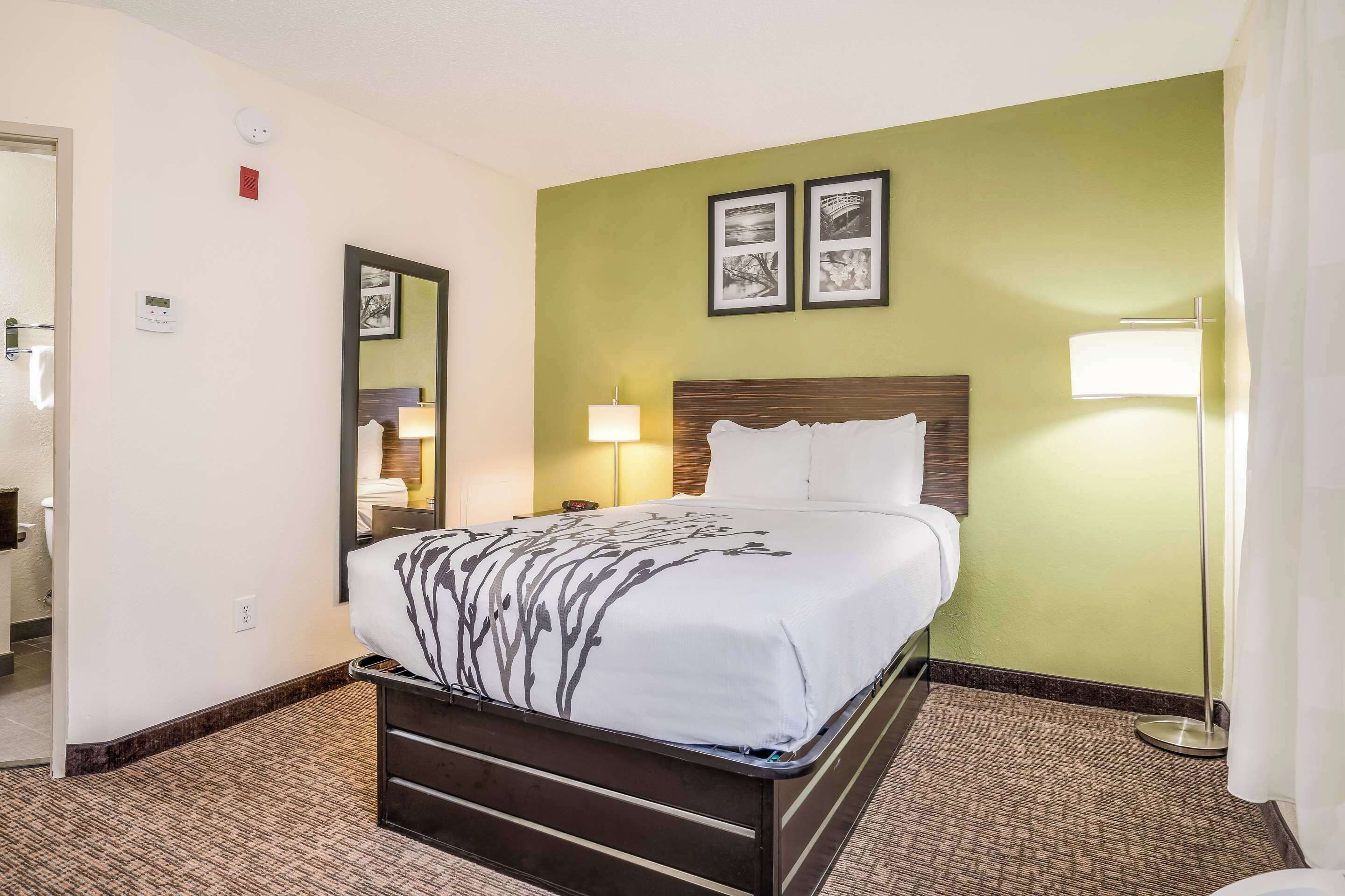 A hotel room with a bed, a nightstand, a lamp, and a wall-mounted mirror.