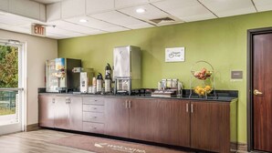 A reception area with a wooden counter, a coffee machine, a water dispenser, and a fruit basket. - Sleep Inn & Suites Jacksonville near Camp Lejeune (Jacksonville)