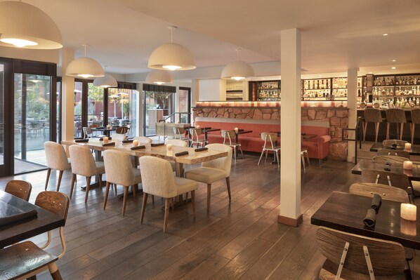 Un restaurante moderno con mesas y sillas de madera, una barra de piedra y grandes ventanales con vistas al exterior.